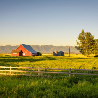 Bild vergrößern: Summer sunset with a red barn in rural Montana and Rocky Mountains