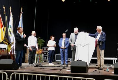 Bild vergr&ouml;&szlig;ern: Im Rahmen des Festakts auf der Hauptb&uuml;hne des Altstadtfests in Mittweida &uuml;berreichte Landrat Helmut Riegger (r.) eine Skulptur von Hermann Hesse, die der Calwer K&uuml;nstler Lothar Hudy angefertigt hat, an Landrat Matthias Damm (2.v.r.).